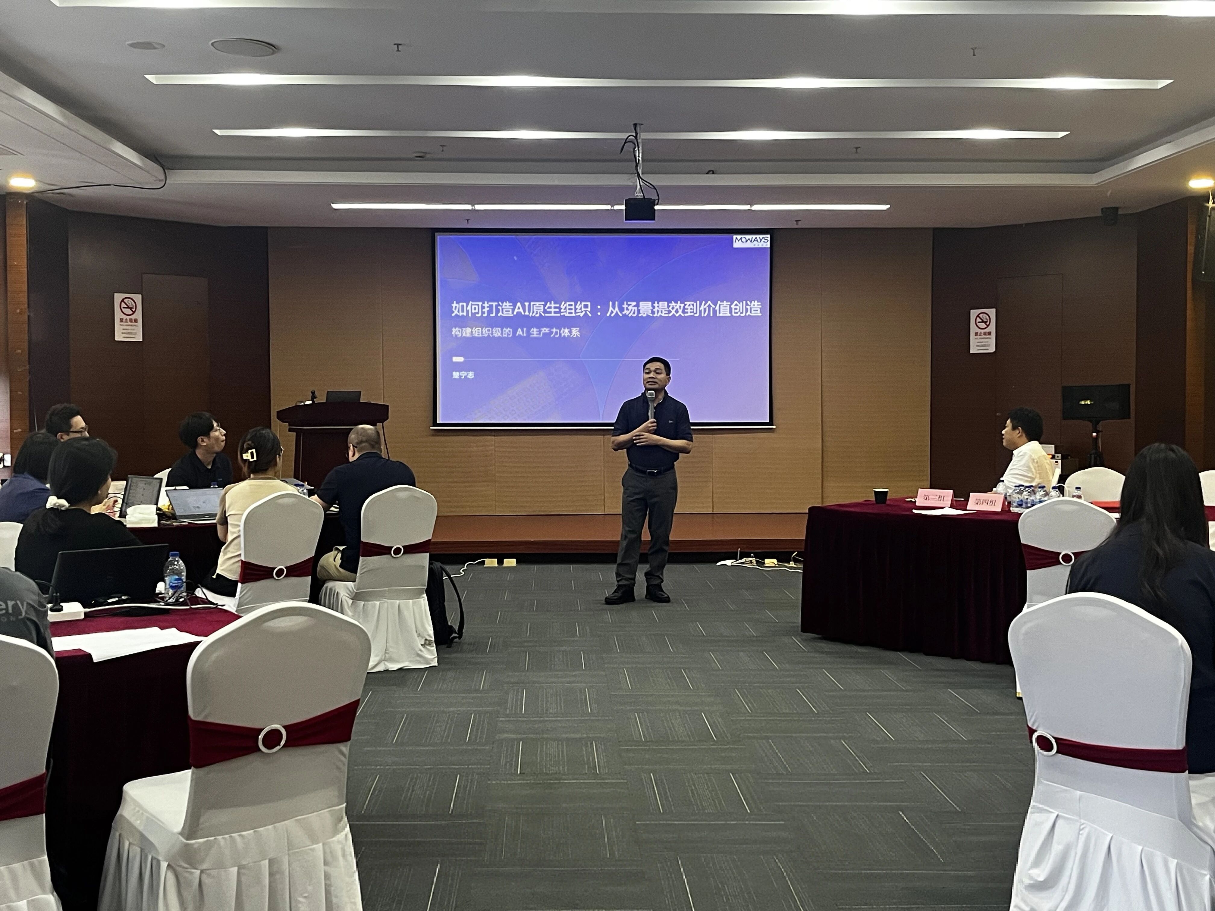 AI训练营会场全景，讲师在大屏幕前授课，参与者围坐在会场中学习