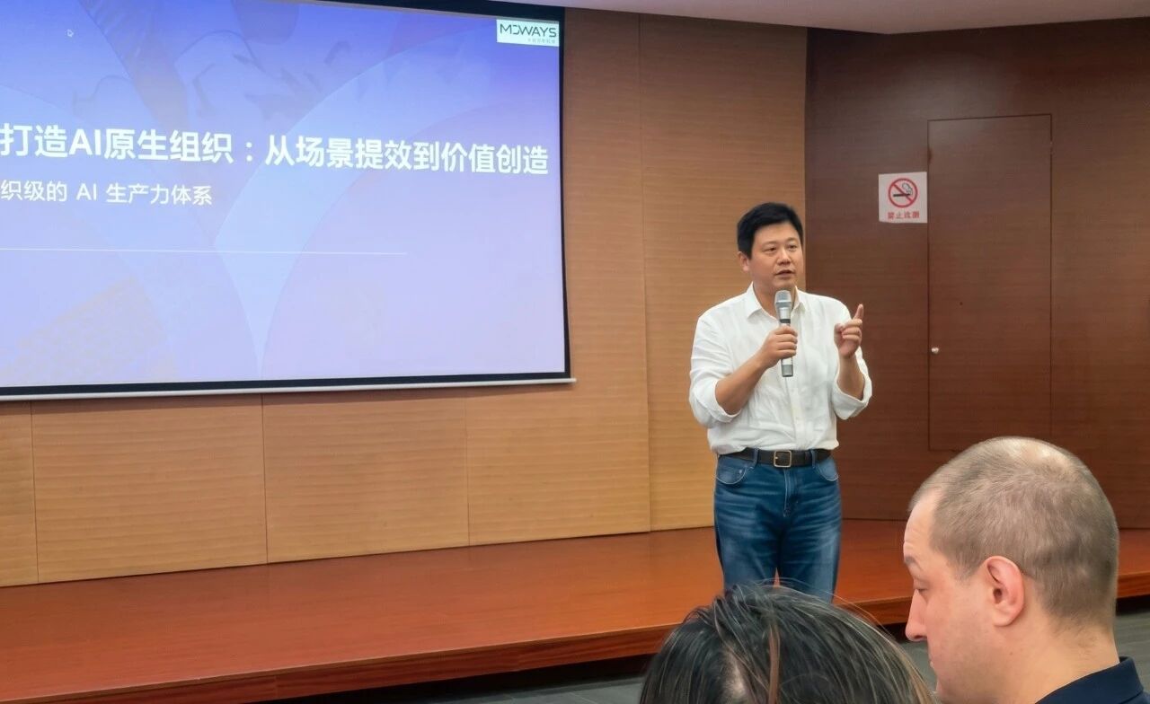 讲师在AI原生组织训练现场使用麦克风讲解，身后是MOWAYS课程屏幕